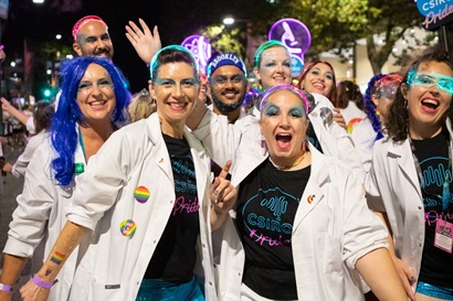 Proud to geek out. Eight people wearing smiles, CSIRO Pride T-shirts, and lab coats at Mardi Gras Parade.
