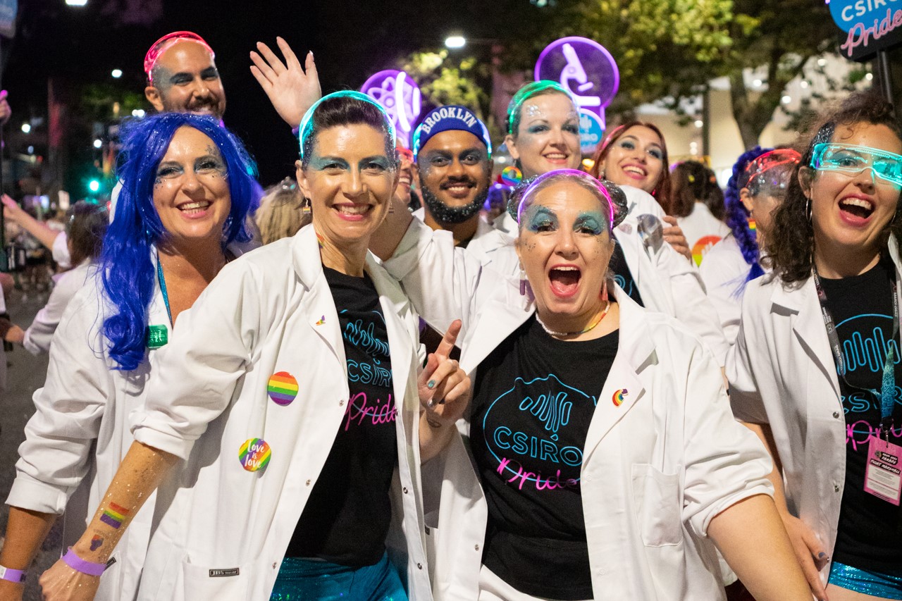 Proud to geek out. Eight people wearing smiles, CSIRO Pride T-shirts, and lab coats at Mardi Gras Parade.