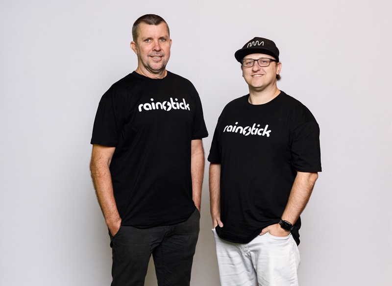 Maiawali man Darryl Lyons and Mic Black standing next to each other wearing t-shirts that read 'rainstick'.