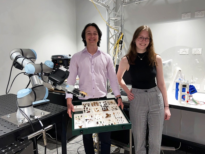 Vacation students Taj and Olivia pictured with their projects, a robot arm holding a butterfly by the pin, and a 3D printed imaging system for digitising insect specimens 