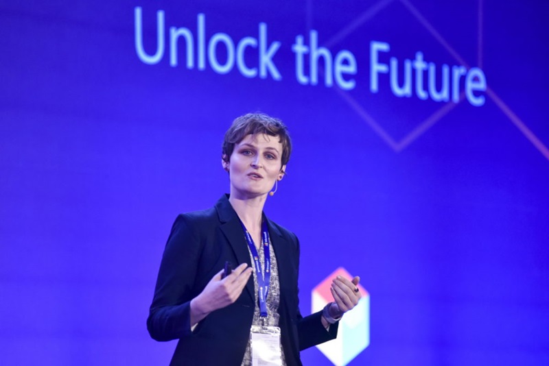 Woman presenting in front of blue screen that says unlock the future.