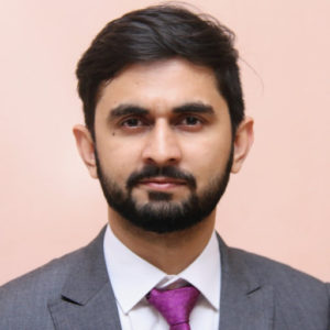 A headshot of Dr Shahroz Tariq, who looks directly at the camera in a suit, in front of a salmon background 