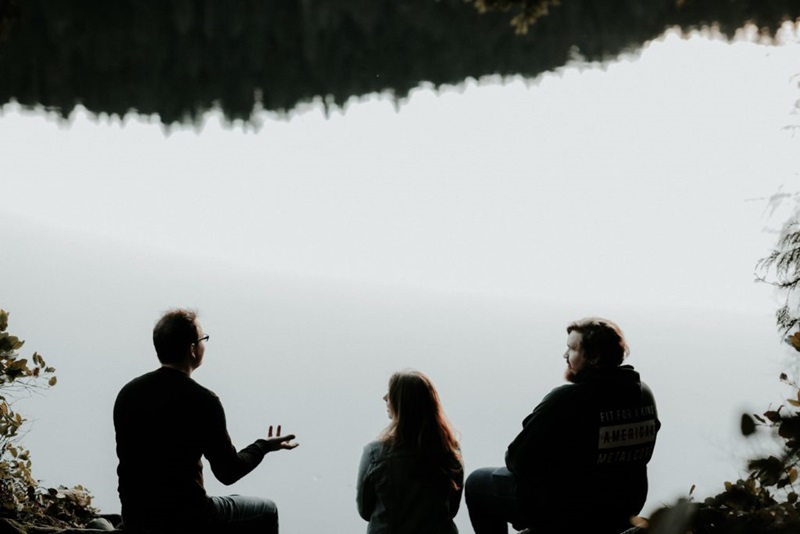 Three people talk while overlooking a lake.