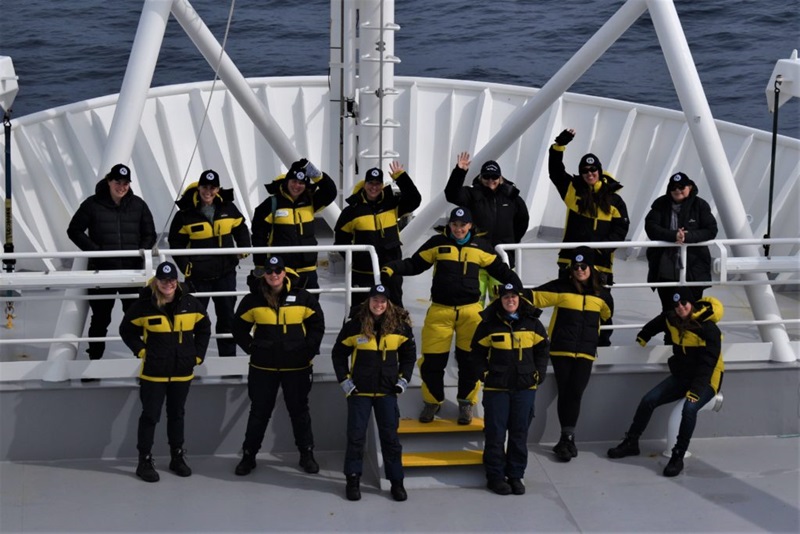 14 women in cold weather gear on a ship