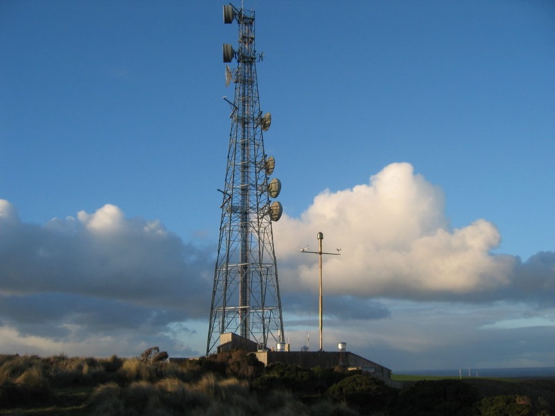 Tall air pollution monitoring metal tower silhouetted against a blue sky.