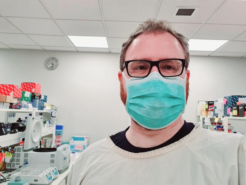 A man in a surgical mask and lab gear.