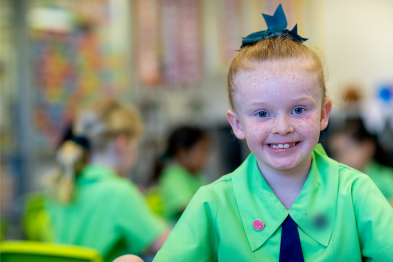 Girl in a school uniform smiling at the camera. Other students can be seen blurred in the background. </p><p>