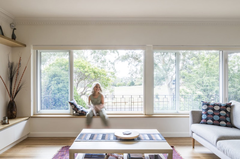 A woman sitting in front of large windows in her home. When renovating or retrofitting ventilation is an important point to consider.