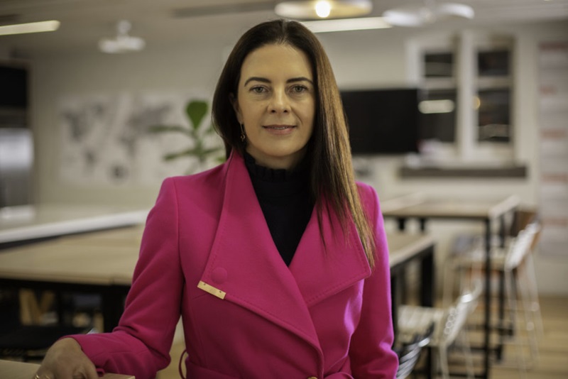 Image of CSIRO's Chief Scientist Dr Bronwyn Fox in a black jumper and bright pink coat standing in an office space. 