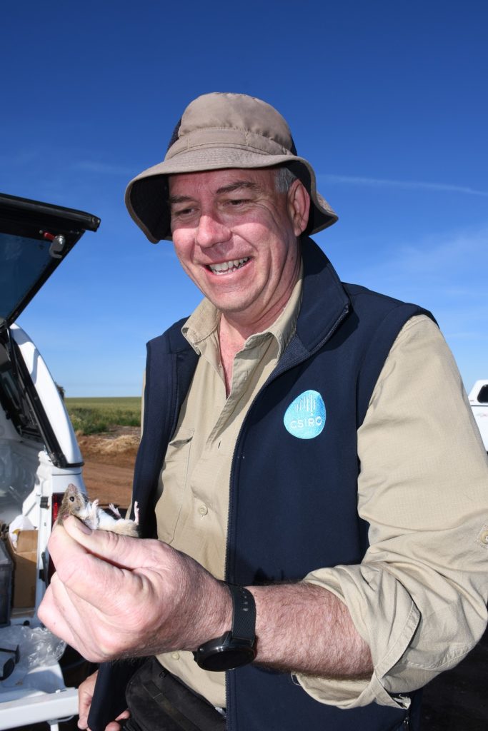 Steve Henry stands in the field holding a mouse.