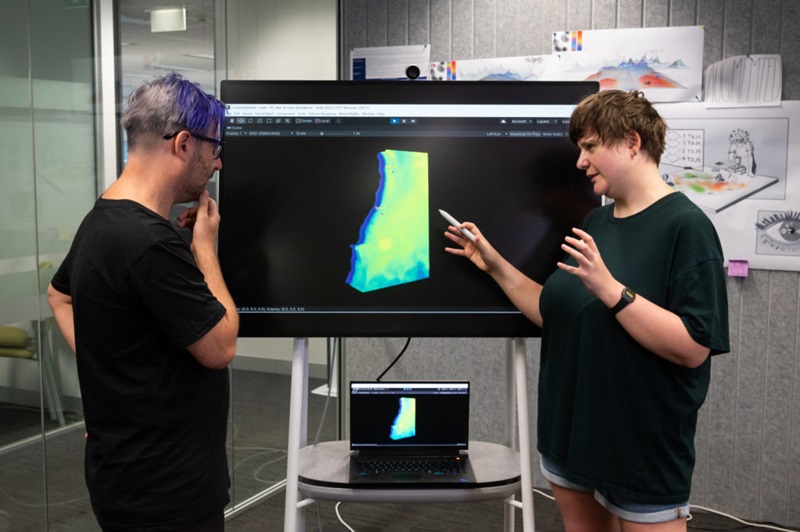 A photo of two people standing and talking infront of a large computer screen which shows a computer-generated map of the ocean using the ocean explorer software.