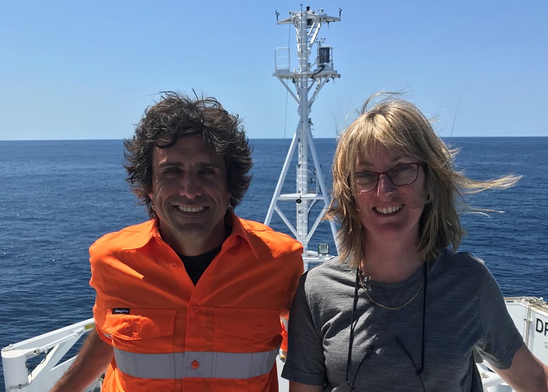 Educators on Board Chris and Greta standing on the ship's bow with a blue sky and the ocean in the background
