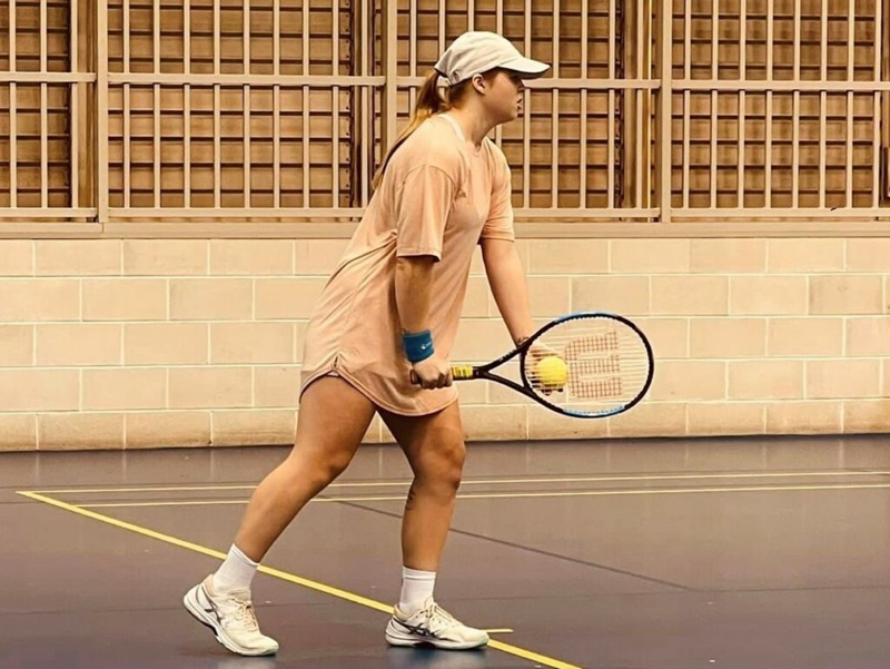 A female tennis player on an indoor court holding a racquet, about to serve