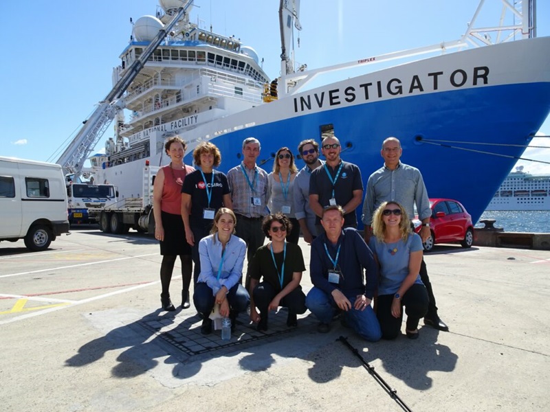 A group of people pose before the research vessel RV Investigator. 