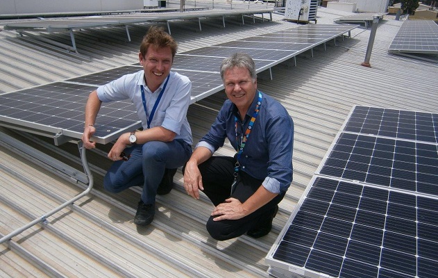 Two men look to the camera near solar roof panels.