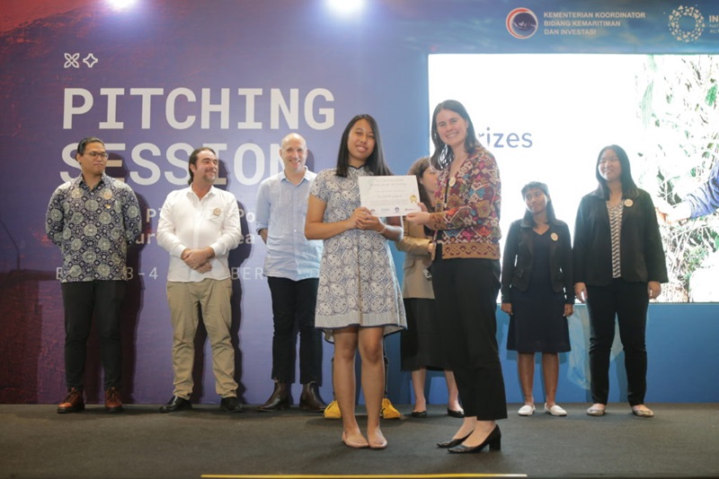 Eight people at an awards cermony. Two women at front of image with award certificate. 