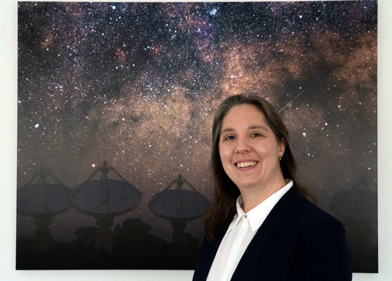 Dr Chenoa Tremblay stands in front of an image of a galaxy