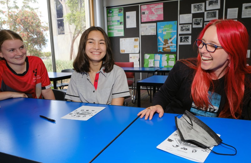 Dr Megan Sebben participating in STEM programs in schools. She sits at a blue table with students in a classroom laughing.
