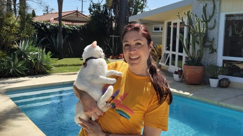 Eleanor stands in front of a pool carrying a squirming cat.