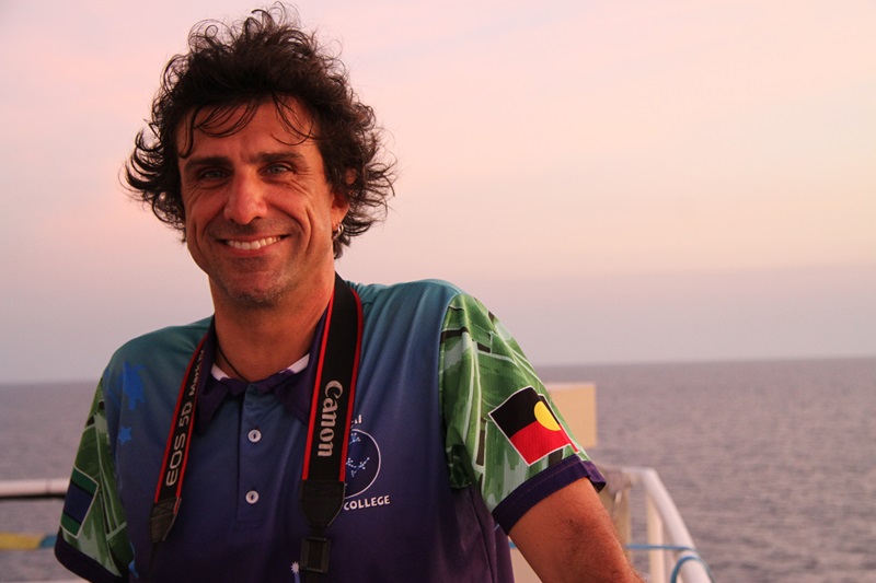 Educator on Board Chris La Rosa standing on the ship with a sunset over the sea in the background