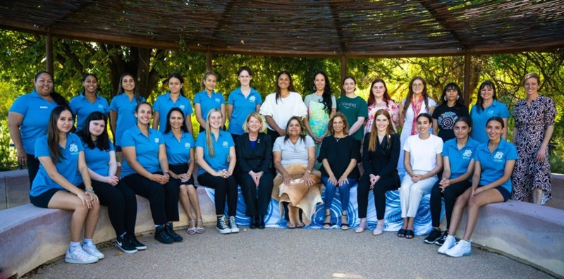 A photo showing a large group of mixed-age women sitting in a semi-circle and looking into the camera. 