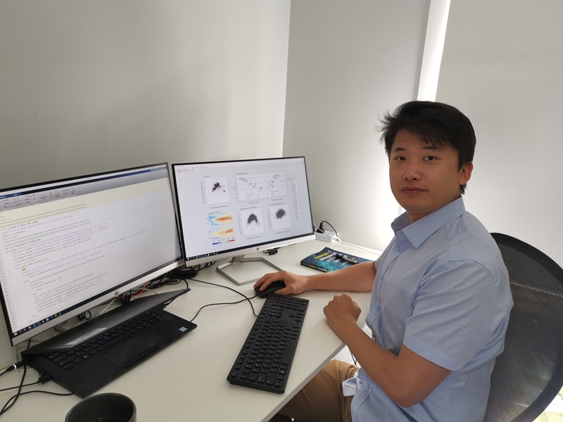 Guojian at his computer smiling at camera. 