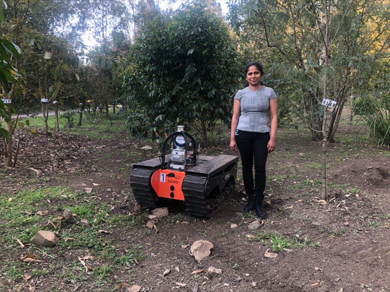 Hashini Senaratne standing next to a robot in a forest. 