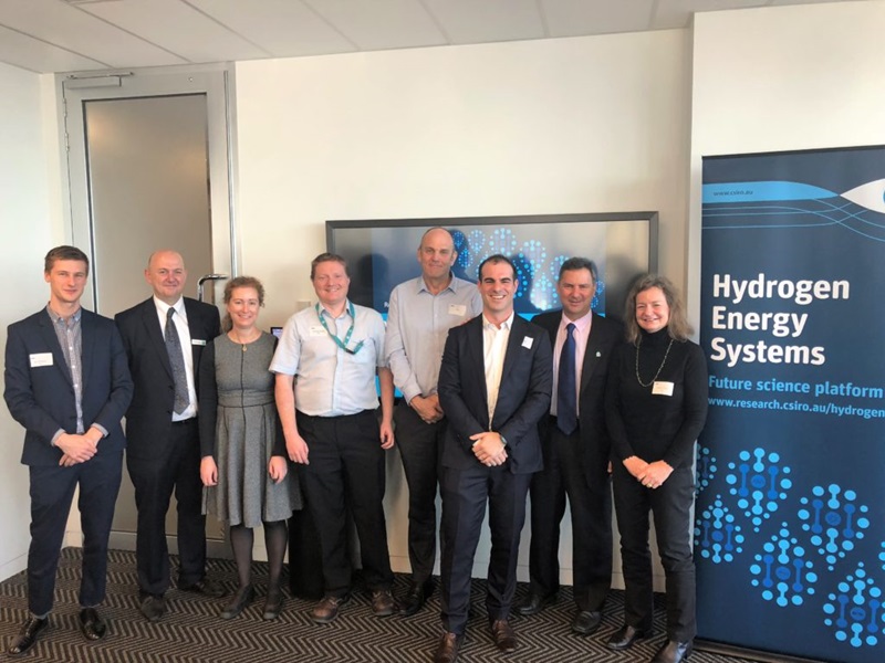 Group of people standing together next to large poster for the Hydrogen Energy Systems.