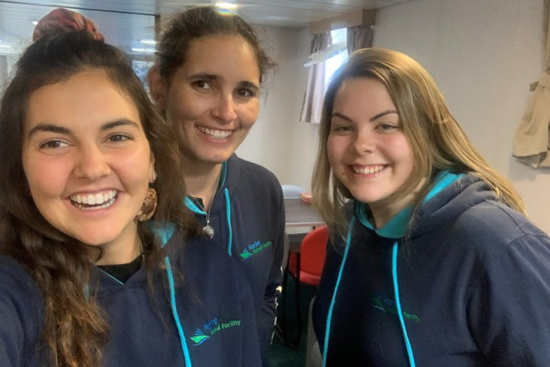Three people wearing matching blue jumpers looking into the camera and smiling.