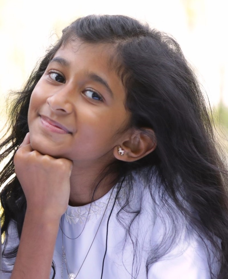 Young girl smiling at the camera while resting her head on her hand.</p><p> 