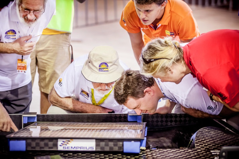 Man surrounded by students looking over a solar panel