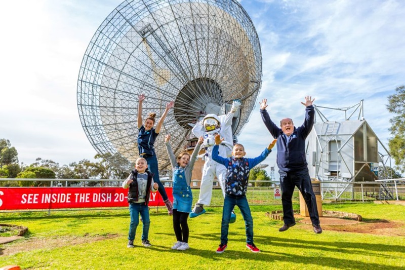 A group of kids jumping for joy on the lawns in front of the Parke radio telescope.