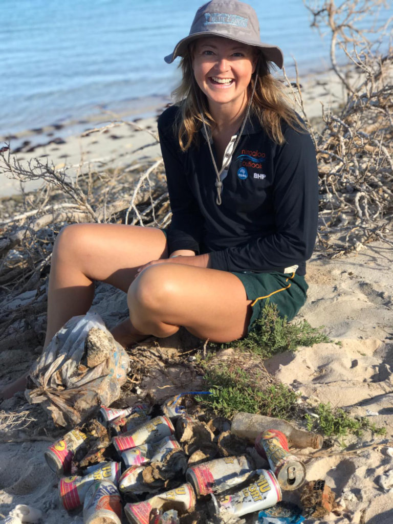 A researcher sitting on the sand of a beach among various items of found litter.