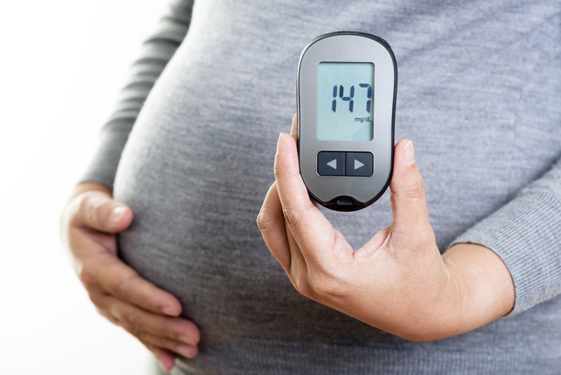 Close up of a person's pregnant belly. The person is holding a device that shows blood suagr levels for those with diabetes