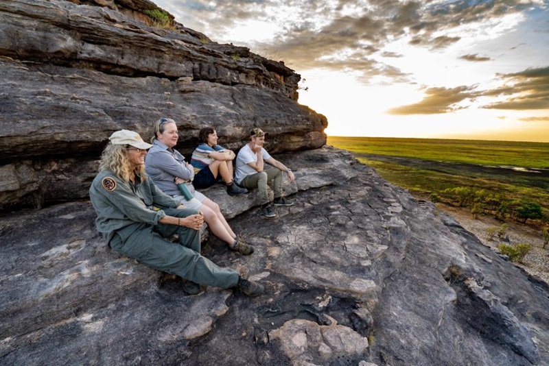 Four people sitting on a rocky outcrop, looking out to the wetlands of Kakadu.