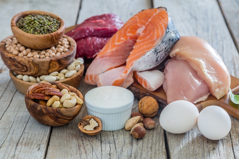 Healthy sources of protein including eggs, fish, nuts and chicken are piled in bowls and a wooden board. 