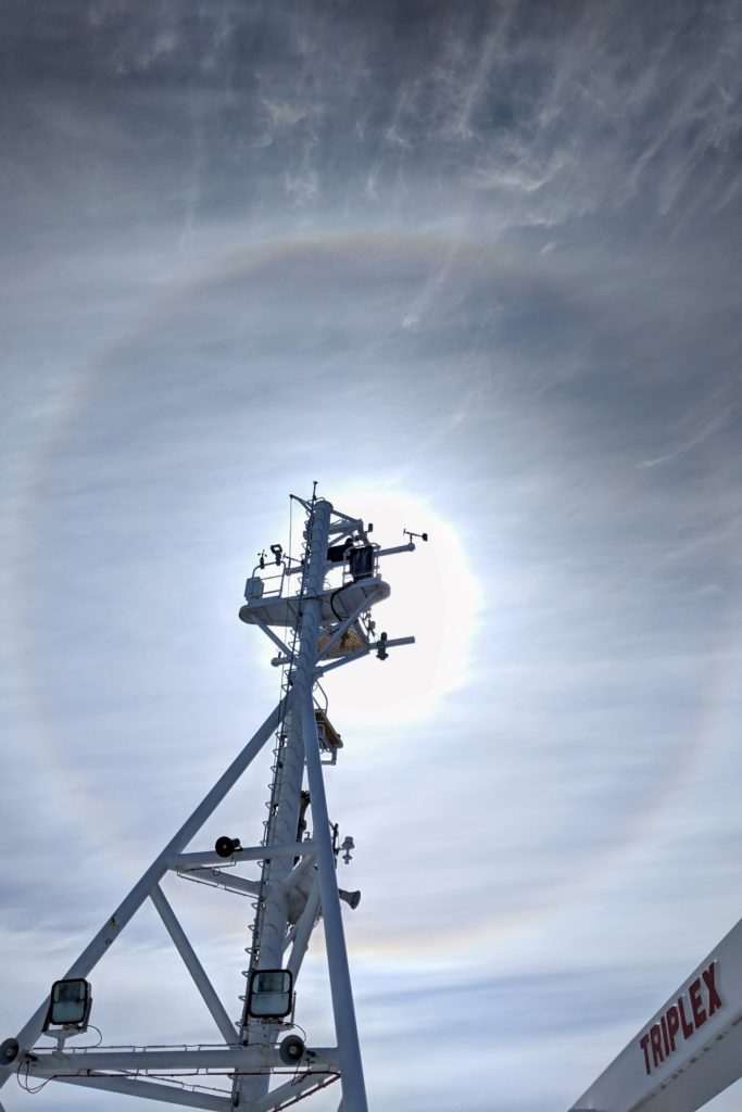 A mast on a ship silhouetted by the sun behind.