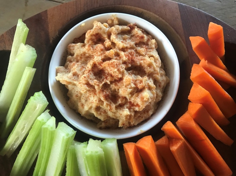 bowl of red lentil hommus surrounded by carrot and celery sticks