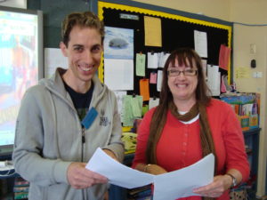 A man and a woman stand teaching science in schools and smiling at the camera.