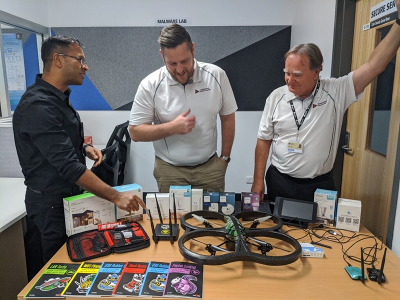 Three men looking at a table of robotics.