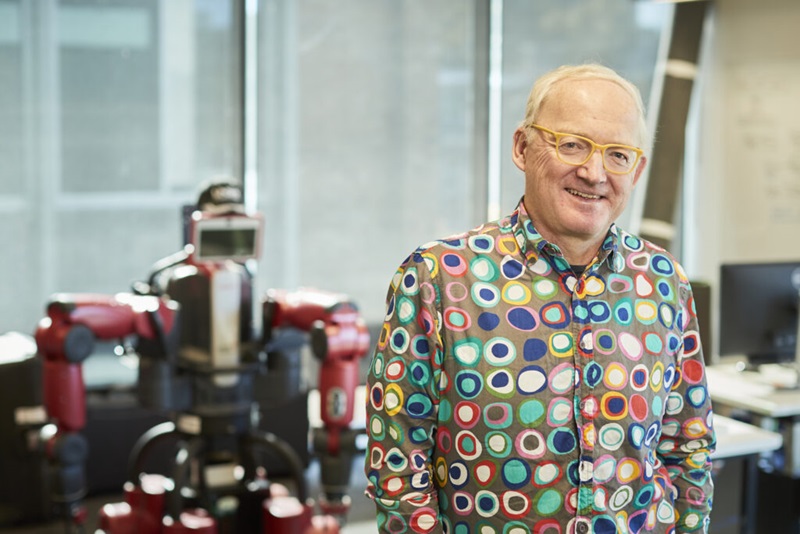 A man in a bright shirt smiling, standing next to a robot
