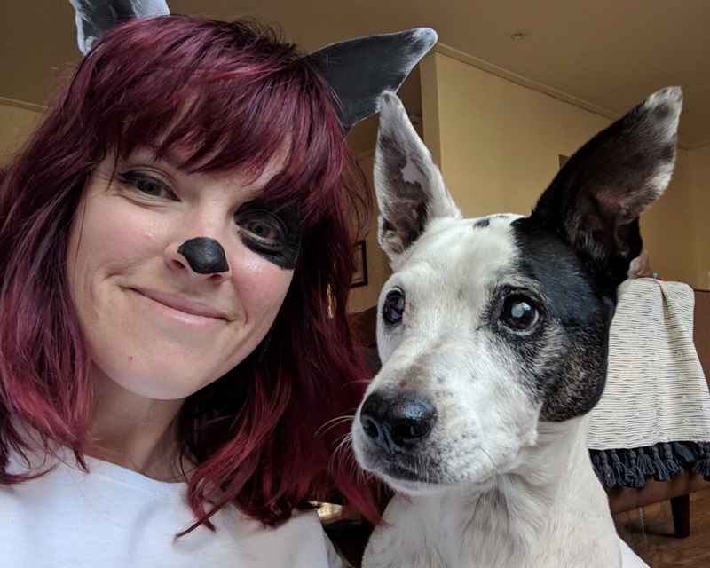 Virginia is pictured with her black and white dog. She is wearing dog ears and has her nose and a patch around her eye painted black to match her dog