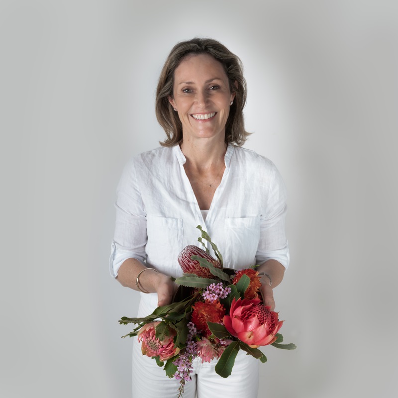 Belinda wearing all white holding a pink bouquet of Australian native flowers.  