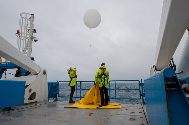 Storm chasing scientists release a large white balloon from the back deck of a ship at sea.
