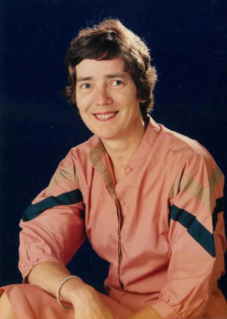 Portrait of woman with short brown  hair in orange jumpsuit smiling at camera. 
