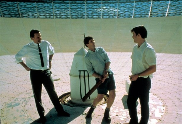 Scene from The Dish movie showing three people playing a game of cricket on the inside of a radio telescope dish. 
