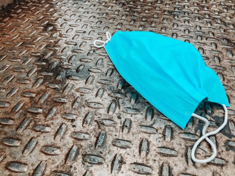 A blue facemask sits on a metal floor.