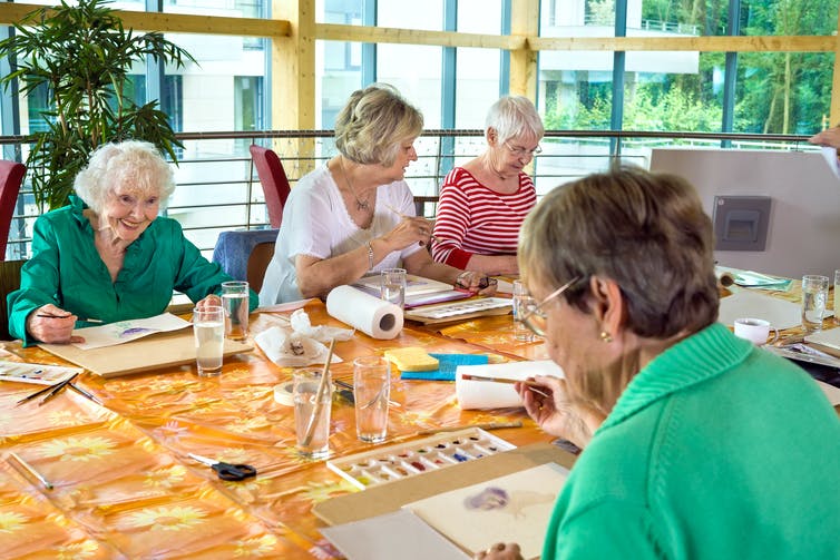 Four elderly women sitting around a table painting with watercolours. Nutritional food swaps.
