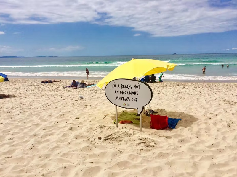 A photo of a beach with a sign in the sand reading "I'm a beach, not an enormous ashtray, ok?"