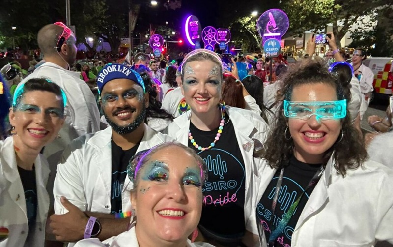 Proud to geek out. Five people wearing smiles, CSIRO Pride T-shirts, and lab coats at Mardi Gras Parade. 